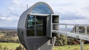 A modern, spherical building with a glass viewing platform extending from its side, overlooking a scenic landscape. - The Skybarrel (Buninyong)