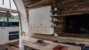 A modern kitchen with wooden cabinetry, a large TV, and a dining area with a table and chairs. - The Skybarrel (Buninyong)