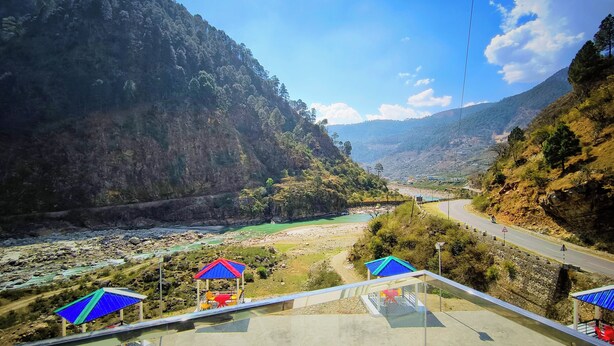 Een prachtig uitzicht op een bergachtig gebied met een rivier, een weg en een brug met picknicktafels en parasols.