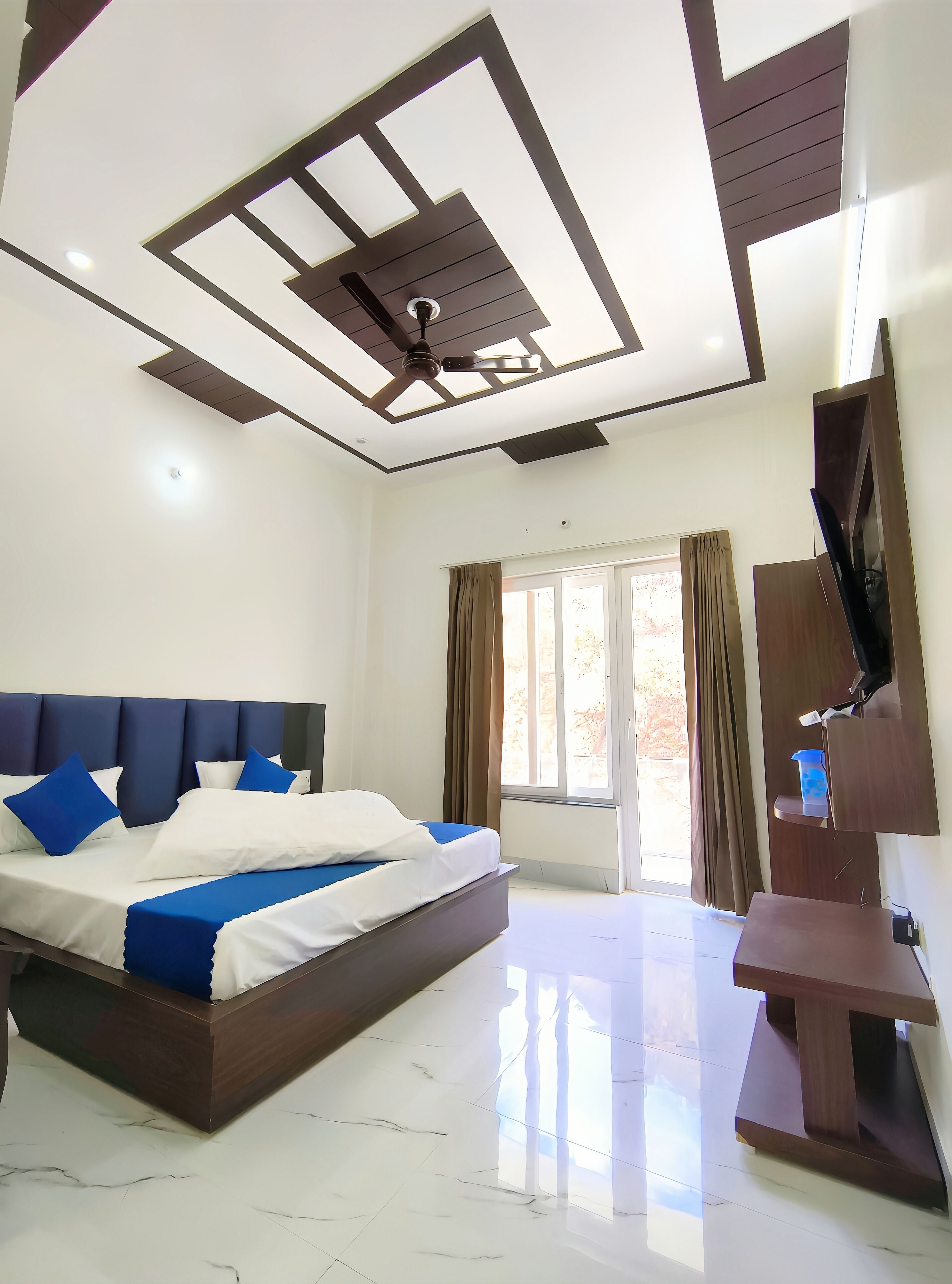A modern bedroom with a large bed, a ceiling fan, and a TV mounted on the wall.