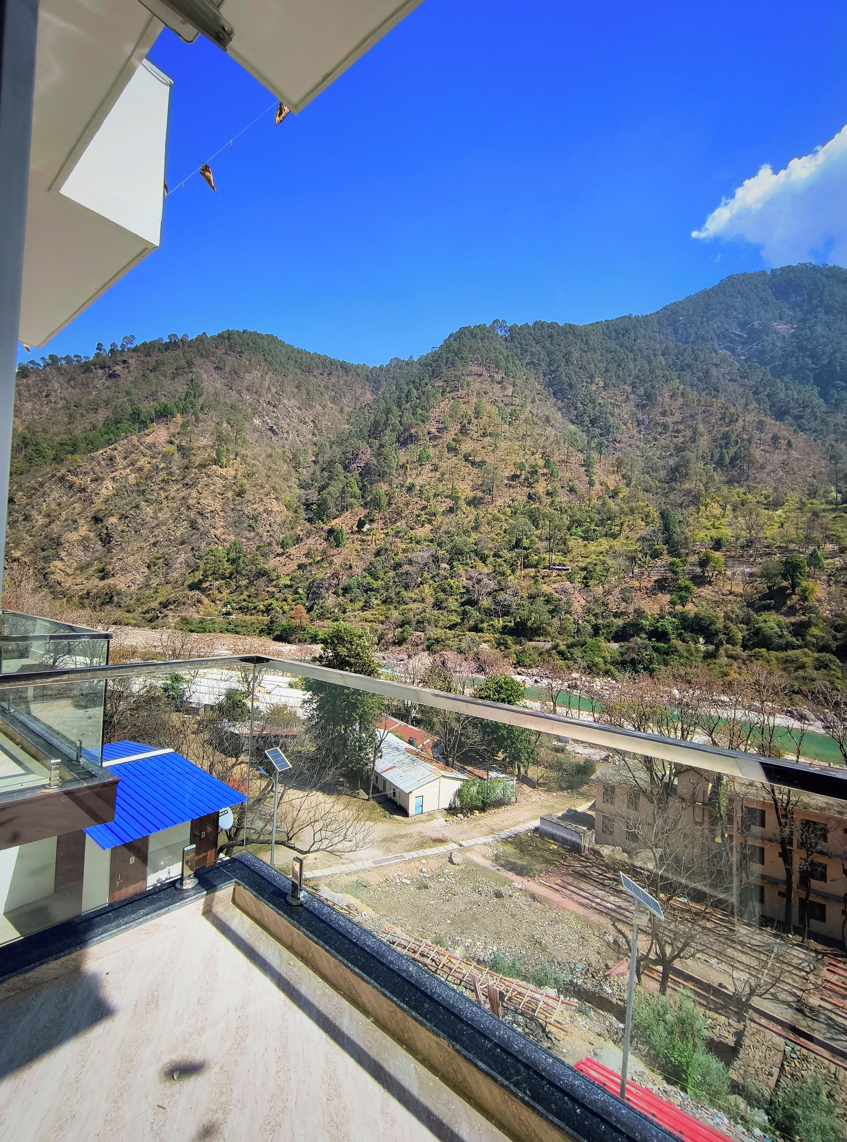 A mountainous landscape with a clear sky, a small building with a blue roof, and a solar panel.