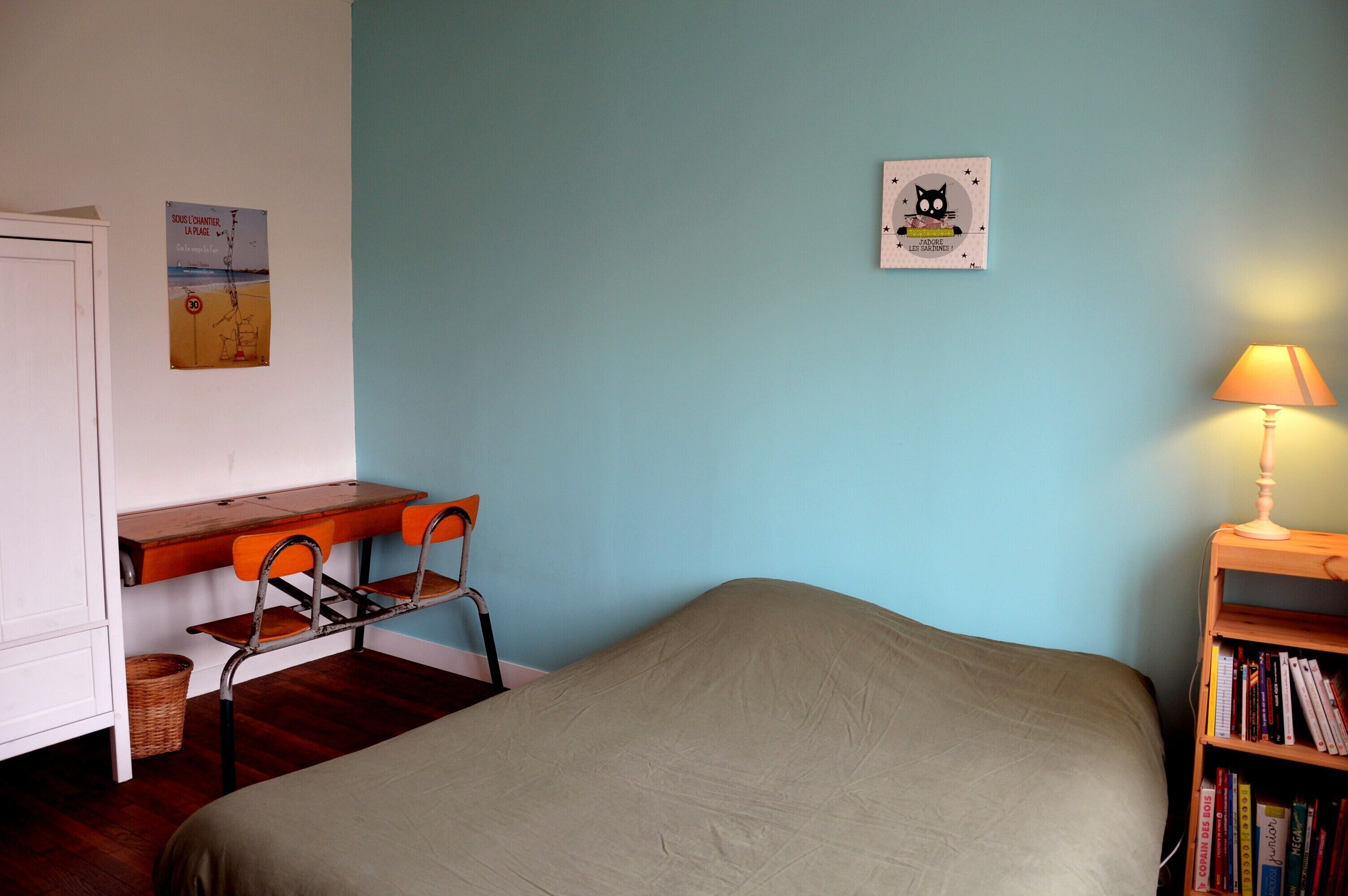 A bedroom with a bed, a desk with a chair, a bookshelf, and two wall decorations.