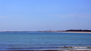 Panorama costiero con un faro in lontananza, mare calmo e spiaggia sabbiosa.