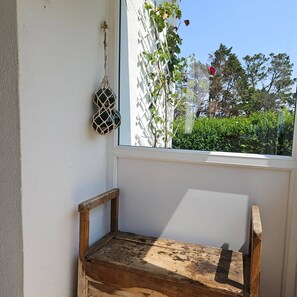 A wooden bench in a corner with a view of greenery and a building outside.