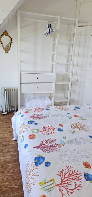 A bedroom with a bed, a white wardrobe, a radiator, and a mirror.