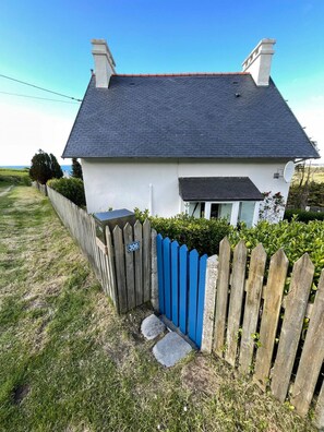 Une maison blanche avec un toit foncé, une clôture en bois peinte en bleu et un panneau indiquant le numéro « 306 ».