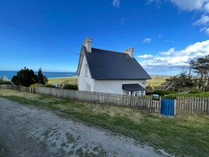 Ein weißes Haus mit dunklem Dach, einem eingezäunten Garten und Blick auf das Meer.