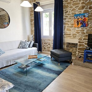 Ein Wohnzimmer mit einer Couch, einem Hocker, einem Glastisch und einer Steinwand.