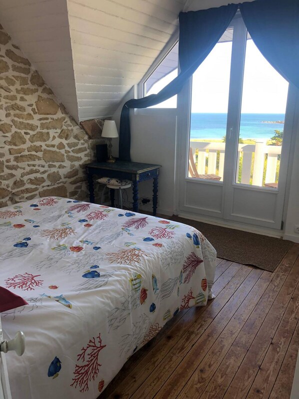 A bedroom with a bed, a nightstand, a lamp, and a view of the ocean through a window.