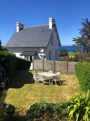A house with a grey roof, white walls, and a fenced backyard with a table and chairs.