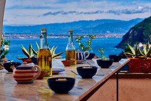 A table with various kitchenware and bottles, overlooking a scenic coastal view. - CASA VACANZE LE TRE SORELLE (Castellammare di Stabia)
