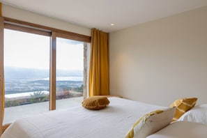 A bedroom with a large window, a bed, and a view of a landscape.