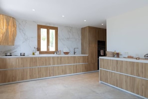A modern kitchen with wooden cabinetry, marble backsplash, and a large window.