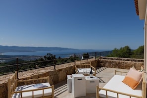 A terrace with a stone wall, a wooden chair, a white sofa, and a table with a bottle and glasses. - Villa ALLEGRIA - Architect-designed villa with infinity pool - Sea  et  mountain views - Sleeps 13. (ALATA)
