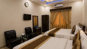 A hotel room with two beds, a flat-screen TV, a desk with a chair, a wardrobe, and a ceiling fan.