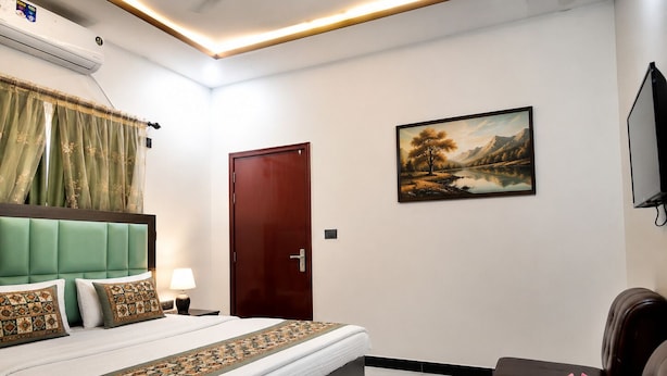 A hotel room with a bed, a desk, a chair, a painting, and a television.