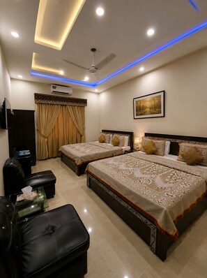 A hotel room with two beds, a flat-screen TV, an air conditioning unit, a ceiling fan, and a framed picture on the wall. - Galaxy Family Hotel (Karachi)
