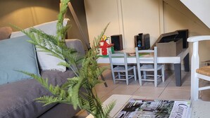 Un salon avec un canapé, une table basse sur laquelle repose un magazine, un vase en verre contenant une plante, une lampe et un escalier en arrière-plan.