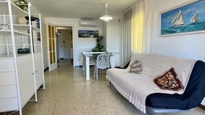 A compact living space with a kitchenette, dining area, and a sofa with a decorative pillow. - JORA 3A (Estartit)