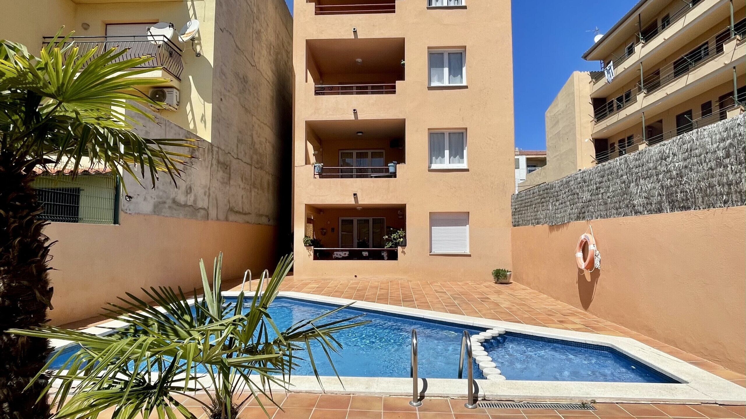 Un immeuble résidentiel doté d’une piscine, de balcons et d’un mur en pierre.
