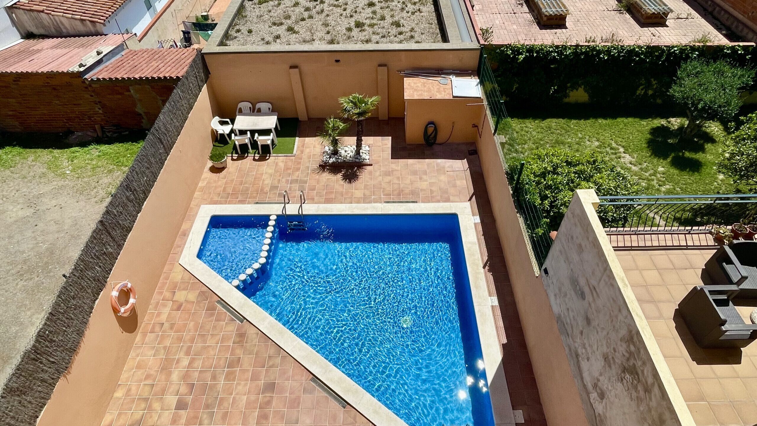 A rooftop swimming pool with a tiled deck, a small table with chairs, and a potted plant.