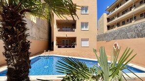 A swimming pool surrounded by a building with balconies and a palm tree.