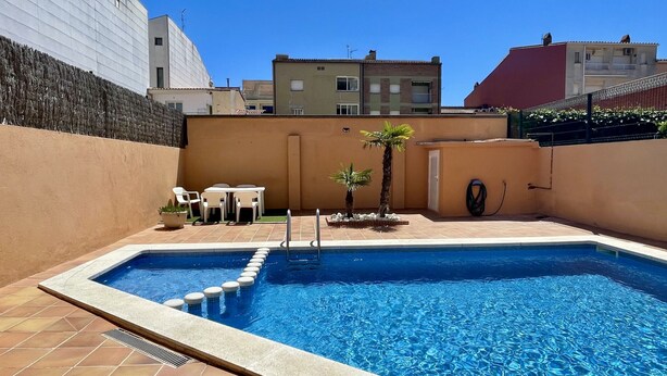 A swimming pool with a tiled deck, a small table with chairs, and a few potted plants. - JORA 3A (Estartit)