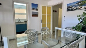 A dining area with a glass table and chairs, a kitchen visible through an open door, and a hallway leading to another room. - JORA 3A (Estartit)
