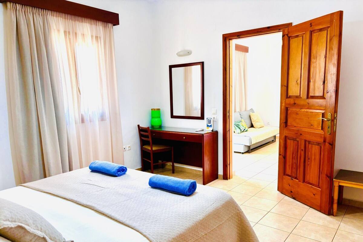 A hotel room with a bed, a desk, a chair, a mirror, and a wooden door.