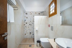 A bathroom with a shower, toilet, and sink, featuring a terrazzo wall and a wooden-framed window.