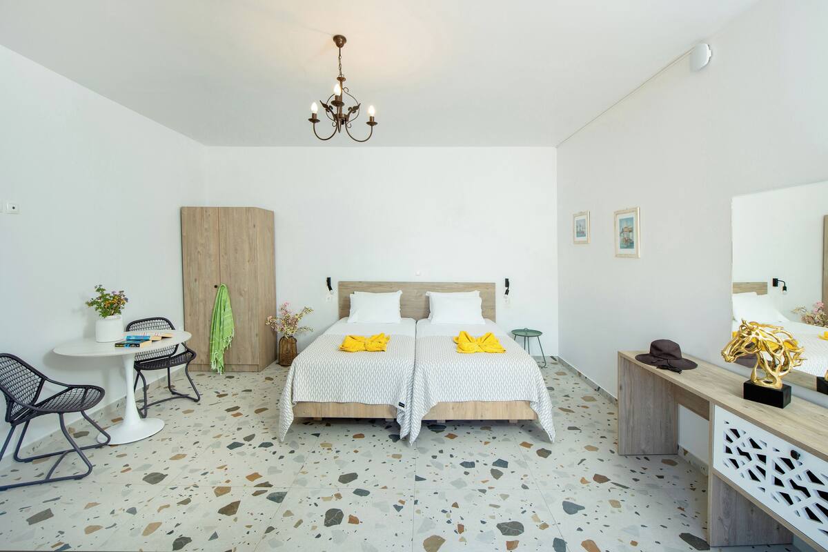 A modern hotel room with a bed, a desk, a chair, a wardrobe, and a chandelier.