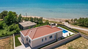A modern house with a red-tiled roof, a swimming pool, and a view of a large body of water. - Villa Eleni ZadarVillas (Ljubač)