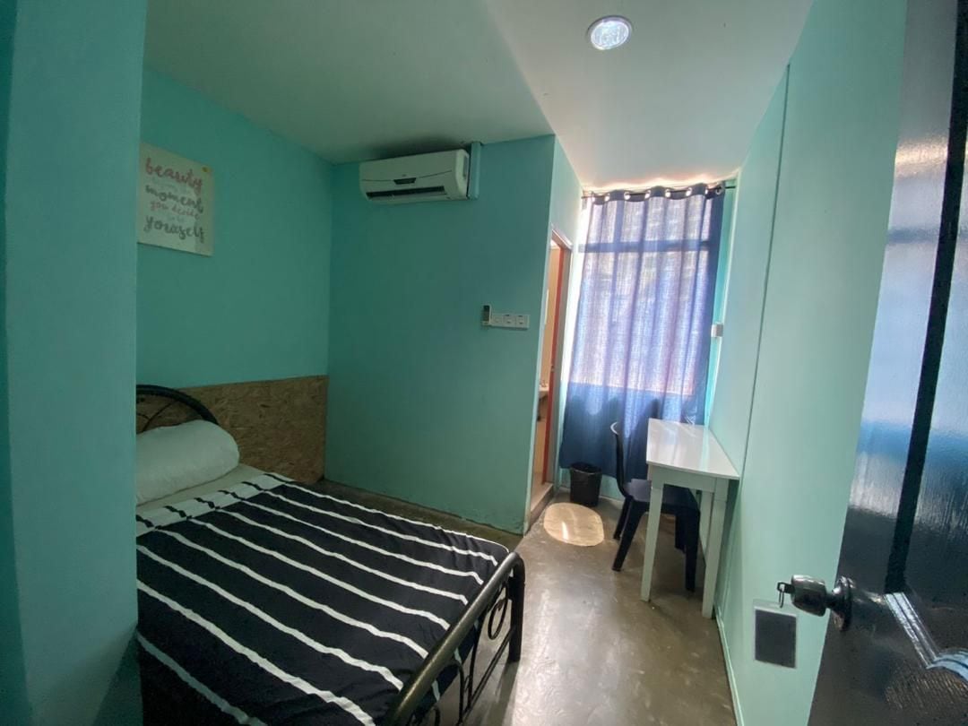 Una habitación pequeña con cama individual, colcha a rayas, escritorio y aire acondicionado.