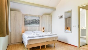 A bedroom with a bed, wooden wardrobe, a painting, a mirror, and a door. - Reevallis Holiday House, Vijlen (Vijlen)