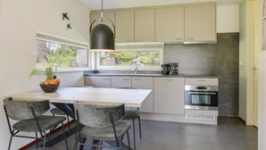 Ett modernt kök med en central köksö, två svarta hänglampor och utsikt över utomhusmiljön genom ett fönster.