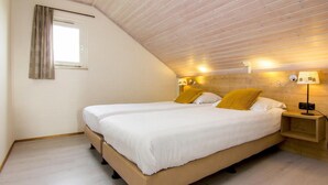Ein Schlafzimmer mit zwei Betten, Holzboden und einem Fenster mit Vorhängen.