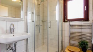 Ein Badezimmer mit einer Duschkabine, einem weißen Waschbecken und einem Fenster über dem Spiegel.
