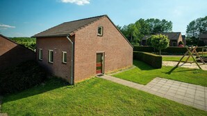Ein Backsteinhaus mit roter Tür und Fenstern, umgeben von einem gepflegten Rasen und einer Schaukel.