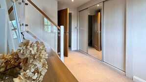 A modern hallway with a wooden bench, a glass vase with dried flowers, and a mirror reflecting the interior.