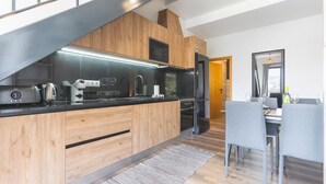 A modern kitchen with wooden cabinets, a black countertop, and a dining area with grey chairs.
