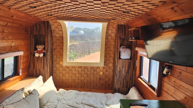 A cozy room with a bed, a window with a view of a landscape, a teddy bear, and a television. - Jeju Pyeongdae 41street Pension (Jeju City)