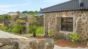 A stone building with a tiled roof, a window, and a garden with various plants and a stone wall. - Jeju Pyeongdae 41street Pension (Jeju City)