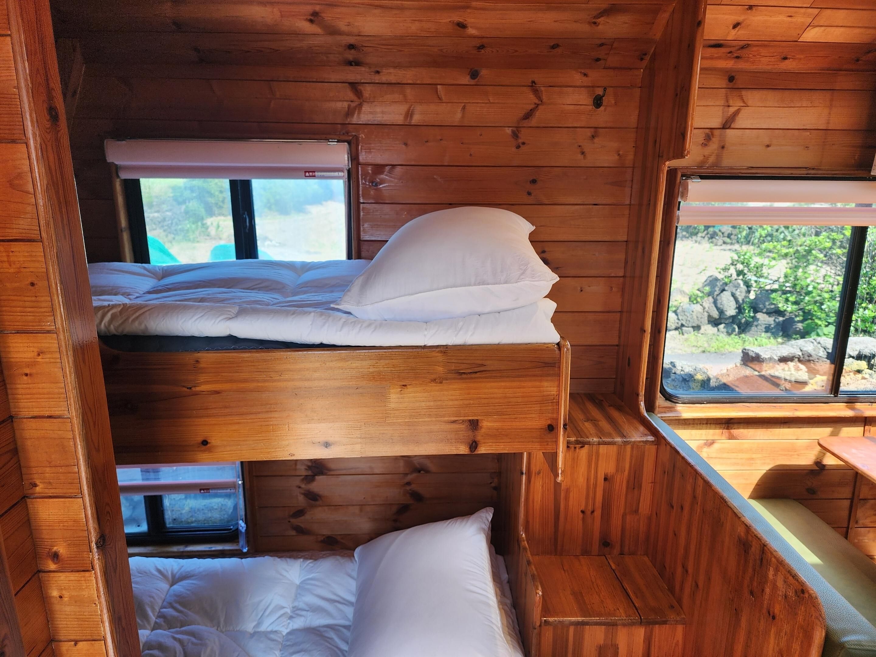 A bunk bed room with wooden walls and a window providing a view of greenery.