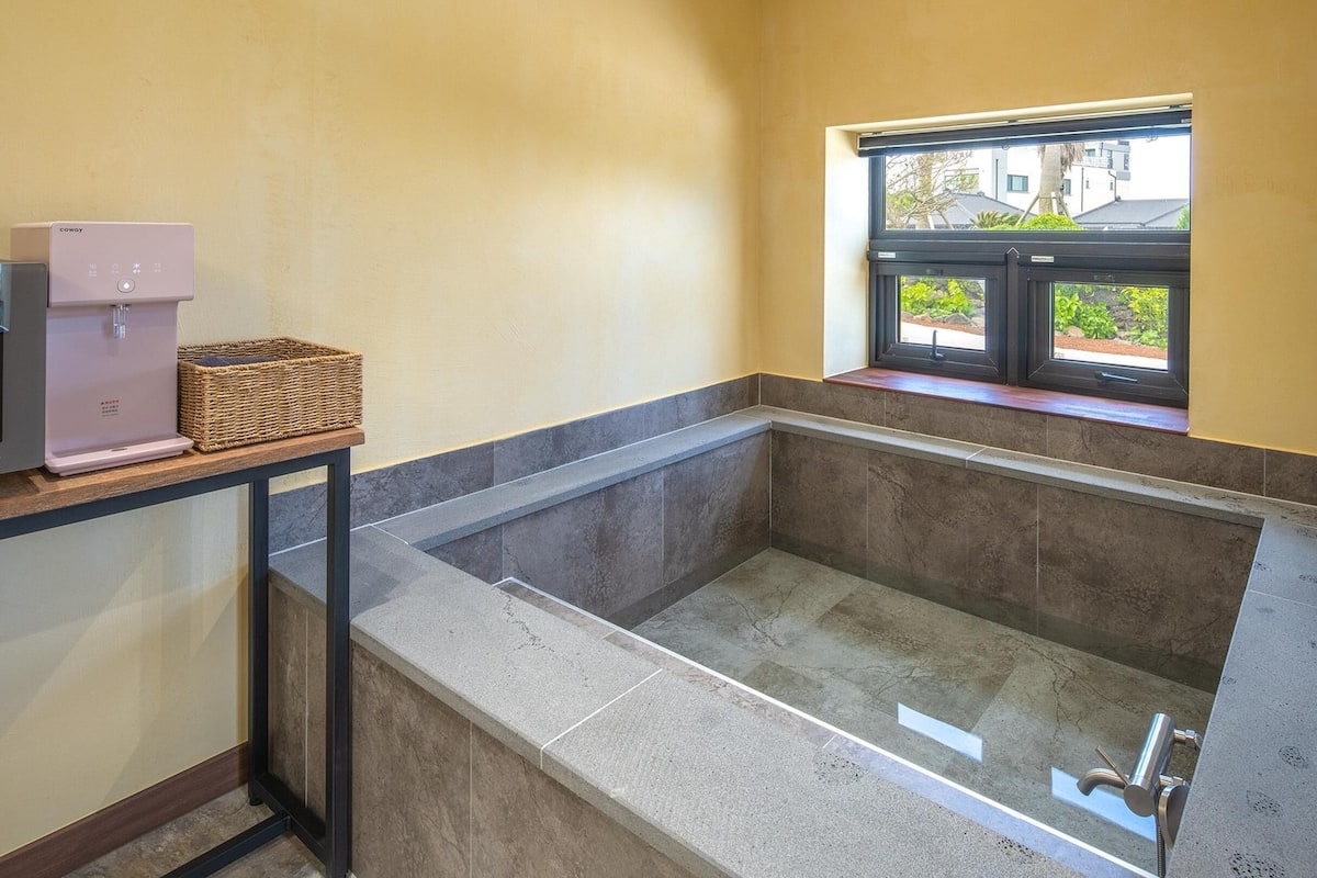 A bathroom with a large bathtub, a window, and a countertop with a coffee maker and basket.
