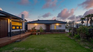 A modern house with a well-maintained lawn, a stone wall, and a wooden deck. - Jeju Pyeongdae 41street Pension (Jeju City)