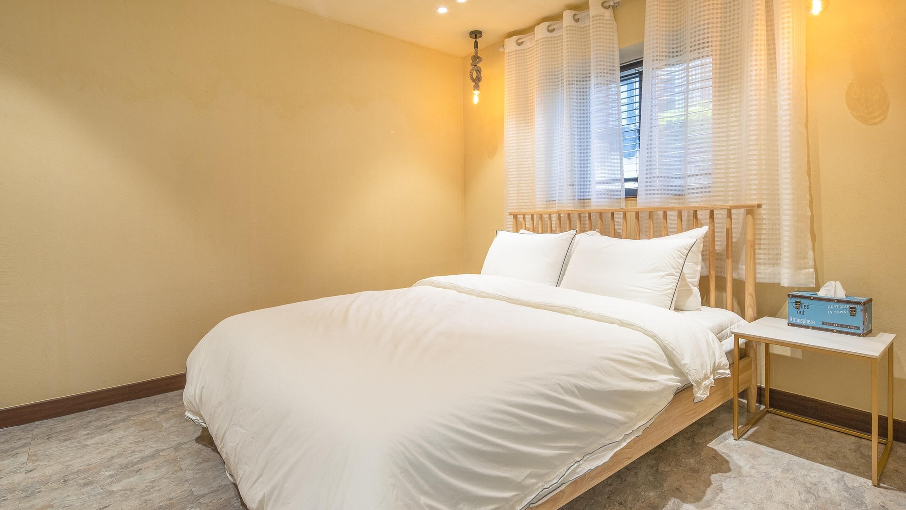 A bedroom with a large bed, a bedside table, and a window with curtains.