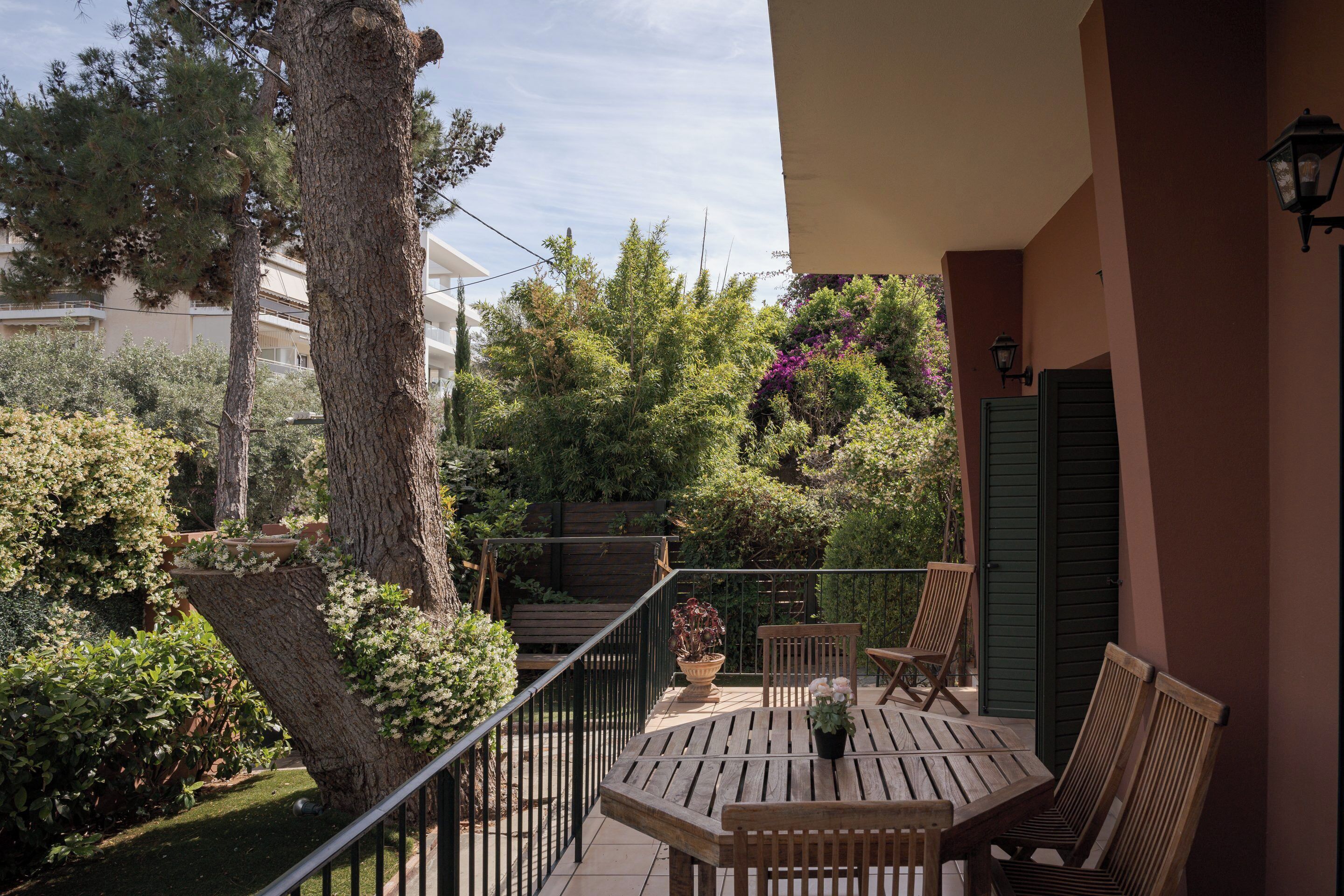 A wooden deck with a table and chairs, surrounded by greenery and trees.