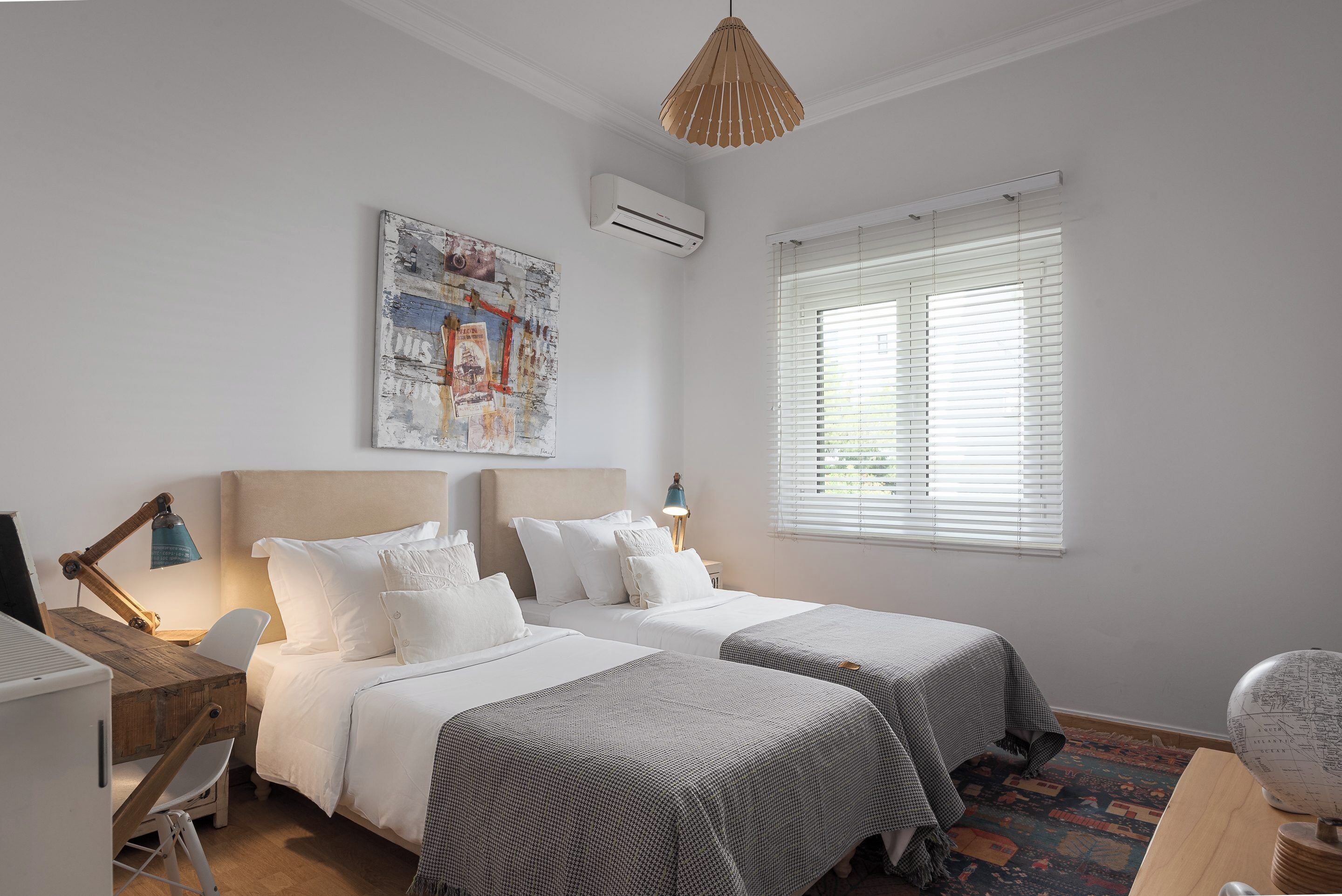 Une chambre avec deux lits, un bureau, une chaise, une lampe, un globe terrestre et une fenêtre avec des stores.