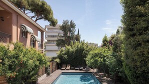 A rectangular swimming pool with a wooden deck, surrounded by lush greenery and trees. - Lussuosa Villa Glyfada (Glyfada)
