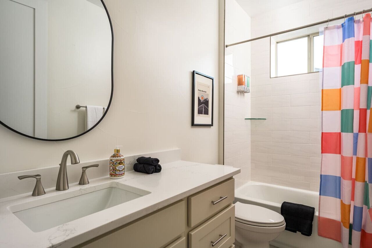 A bathroom with a large mirror, a sink with a marble countertop, a toilet, and a shower with a colorful curtain.